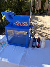Load image into Gallery viewer, A blue snow cone machine with 'Sno-Kones' written on the front, set on a white tablecloth outdoors with soda bottles and cups beside it.